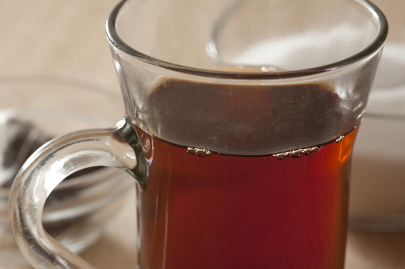 Glass mug of freshly brewed hot black tea , close up view to the rim of the glass and top of the beverage