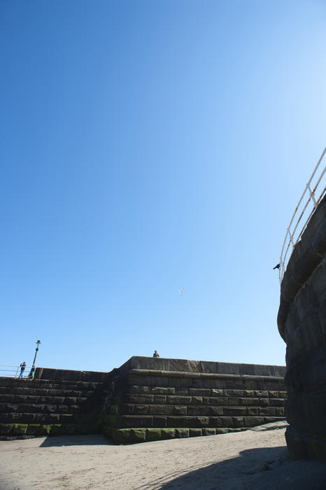 Stone pier and a deserted sandy beach at Whitby under a clear blue sunny sky