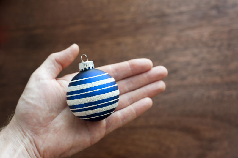 Man holding a blue Christmas bauble in his hand displaying it to the camera over a wooden background