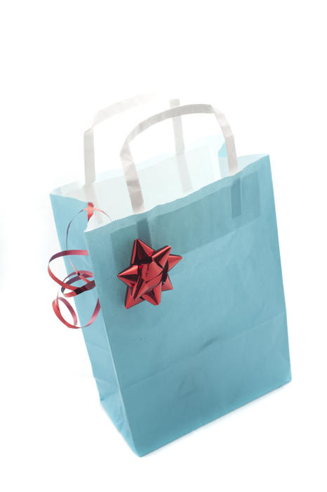 Close-up of a blue gift paper bag decorated with a red shiny bow, on white background, shot from high angle
