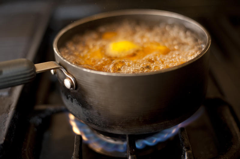 Pot or saucepan with pumpkin or butternut boiling on a gas hob with frothing bubbles and steam