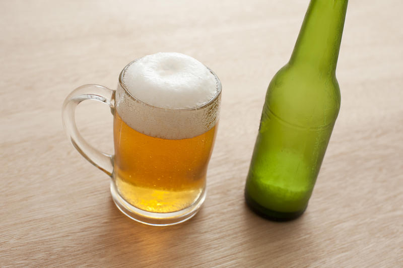 Tankard of frothy cold beer with a green beer bottle standing on a wooden counter, high angle view