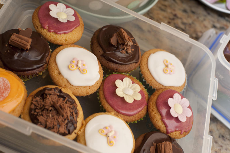 Plastic container filled with colorful cupcakes decorated with butterflies and flowers ready for a childs birthday party