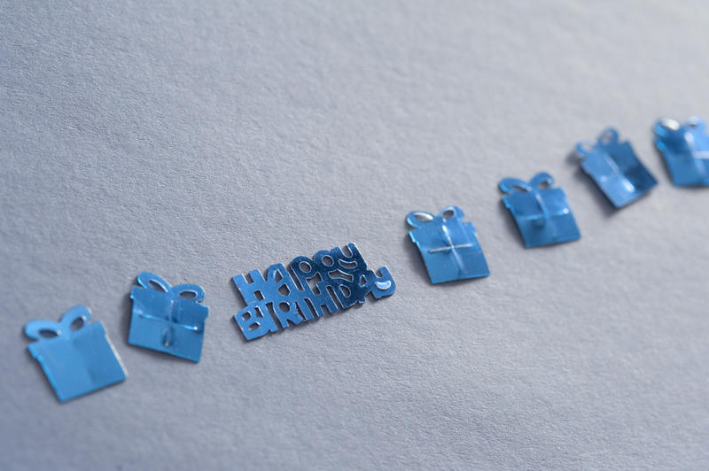 Blue decorative shapes for a birthday boy with a Happy Birthday sign and assorted gift boxes tied with ribbon arranged in a diagonal line over grey with copyspace