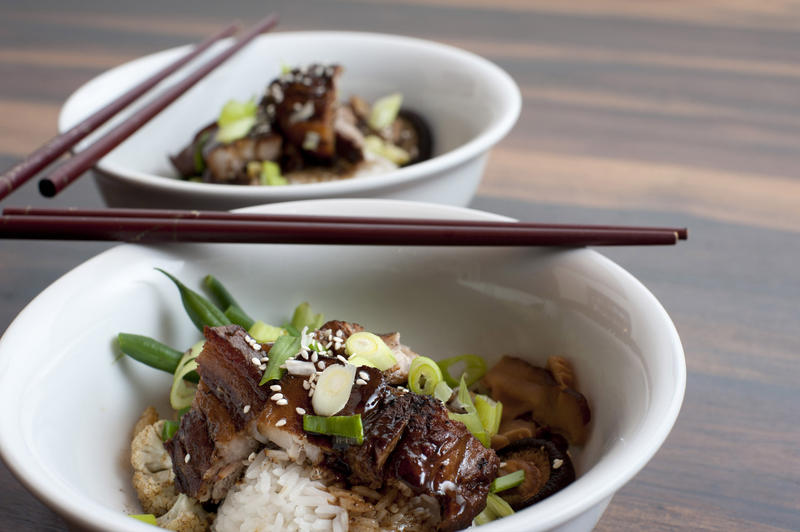 Close up of a bowl of Chinese fatty pork and vegetables topped with a rich sauce and served with chopsticks