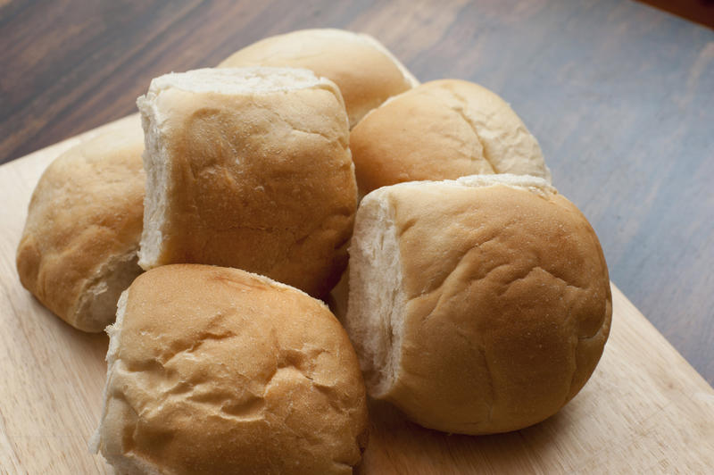 Fresh crusty round white cob rolls in a pile on a wooden bread board, close up view