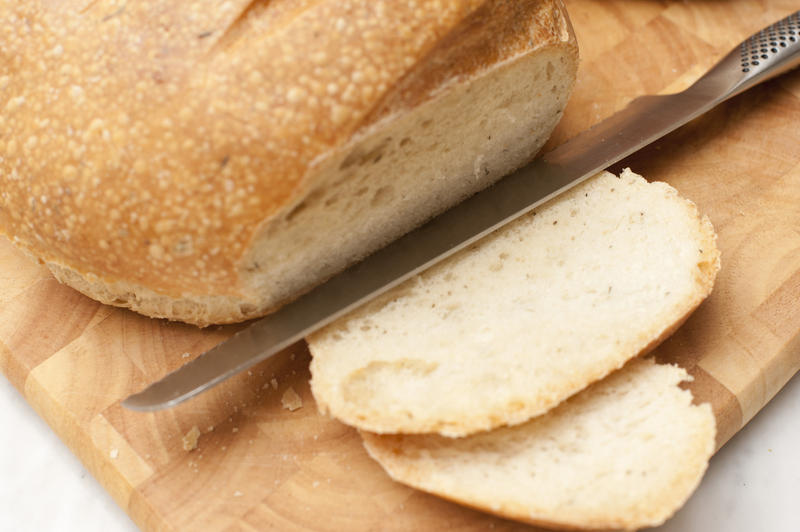 Delicious freshly baked crusty loaf with sliced bread and a bread knife on a wooden board, close up high angle view