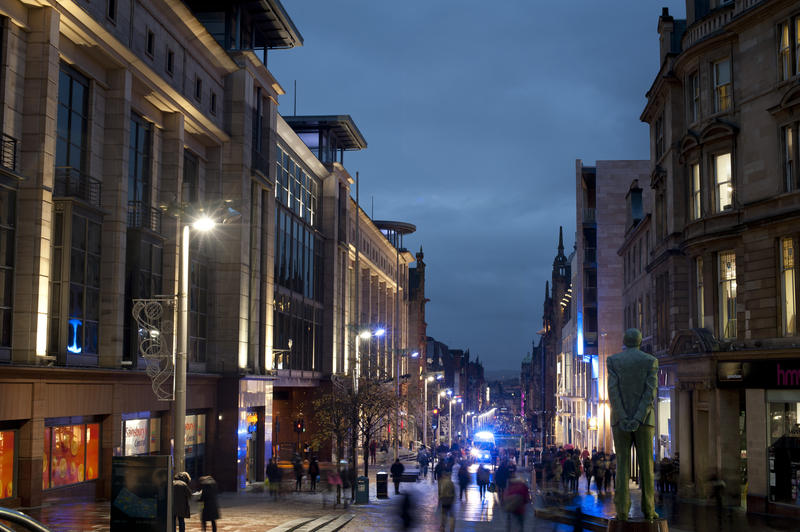 Buchanan Street in central Glasgow at night with shoppers milling the streets lit by the lights from colourful shop windows lining the road
