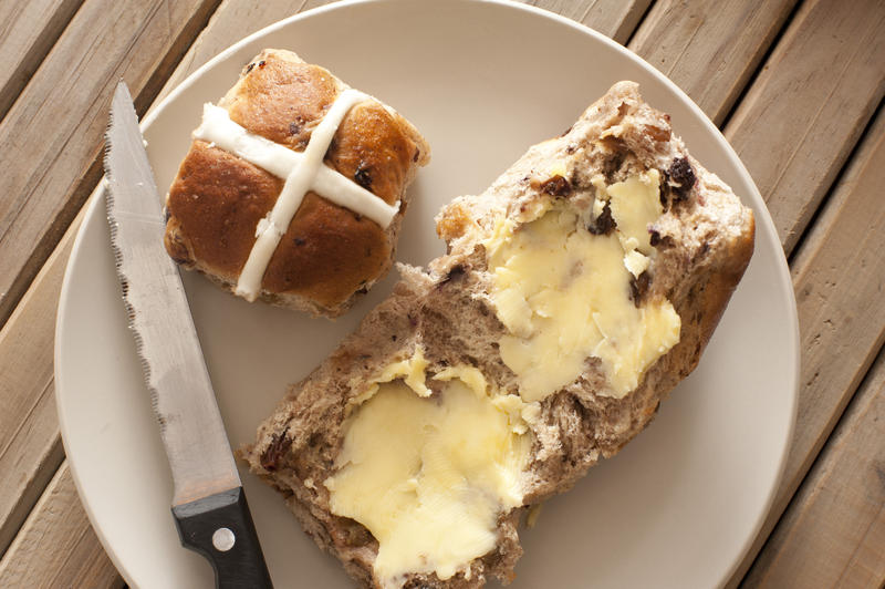 Fresh buttered hot cross bun on a plate with a whole bu showing the cross on top to celebrate the Easter season, overhead view