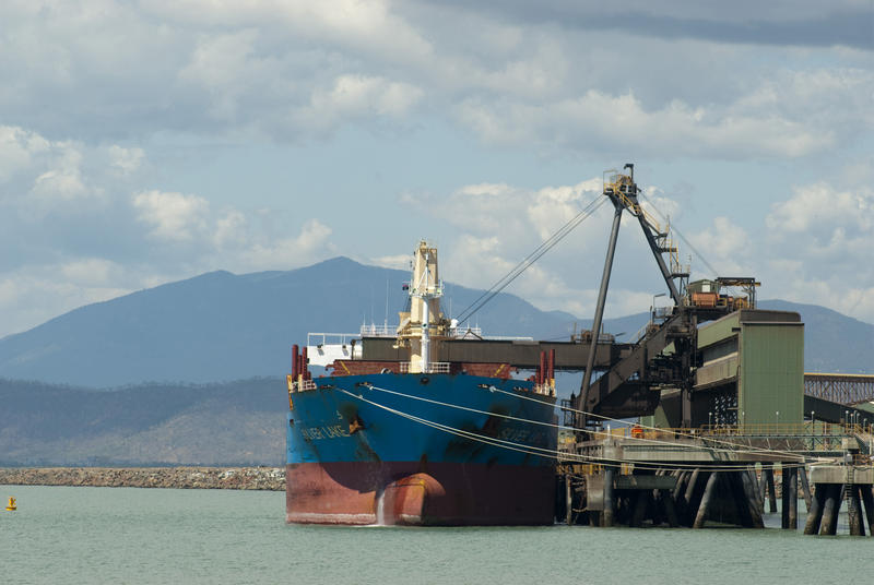 Freighter being offloaded at a cargo wharf in a harbor or port using a crane, front view of the bows