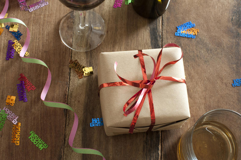 Celebration concept with a gift-wrapped present, alcoholic beverages and party streamer with colorful sprinkles on a wooden table, high angle view