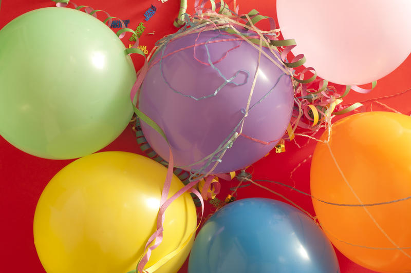 Overhead background view of a bunch of colorful party balloons and streamers for use as celebration decorations on red
