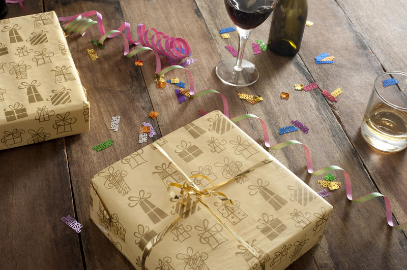 Celebration or party background with decorative gifts, confetti, streamers and alcoholic beverages on a wooden table, high angle view