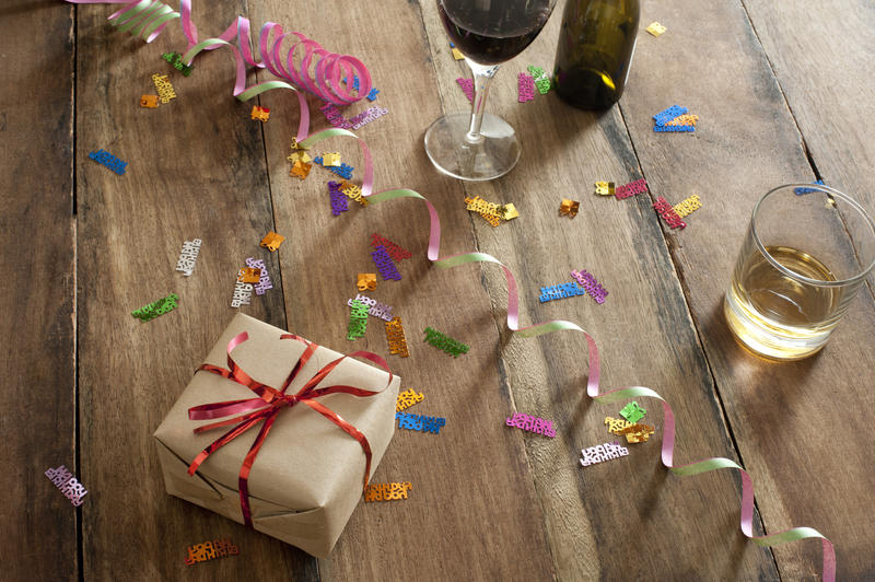 Celebration still life with party streamers, confetti, alcoholic beverages and a gift wrapped with a red bow on a wooden table, high angle view