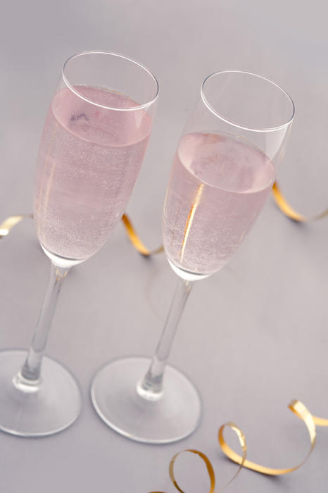 Two elegant glasses or flutes of sparkling pink champagne with a festive twirled gold ribbon for a special occasion or romantic celebration
