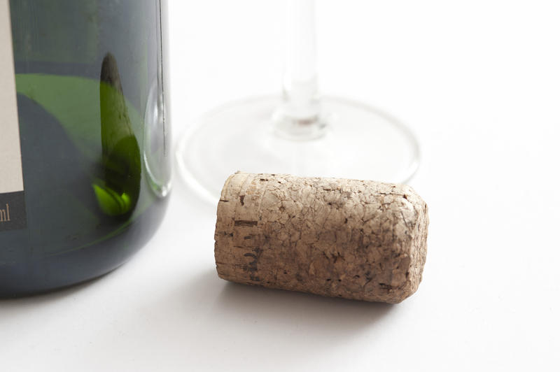 Close Up Still Life of Cork on White Background Beside Green Glass Champagne or Wine Bottle and Wine Glass