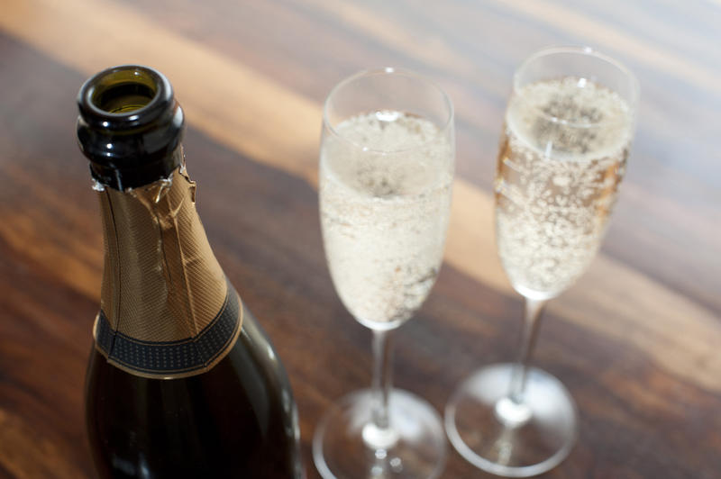 Uncork bottle of champagne and two flutes on wooden table