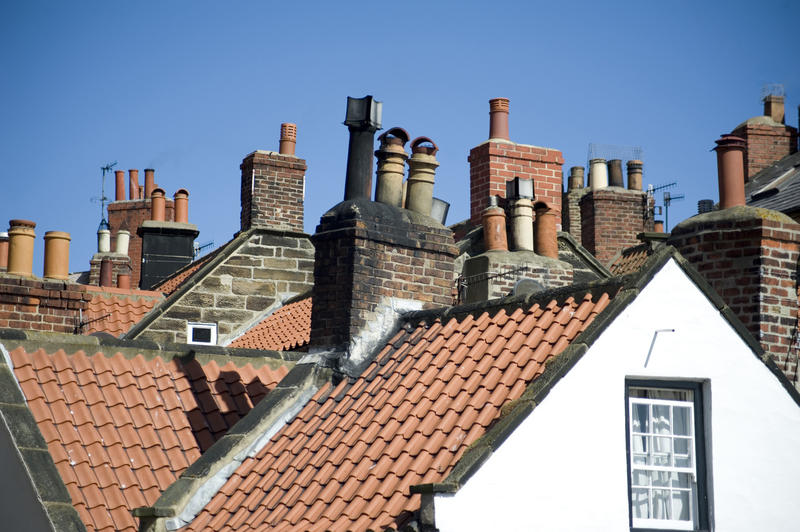 View across typical English cottage rooftops with a variety of chimneys and chimney pots under a blue sky