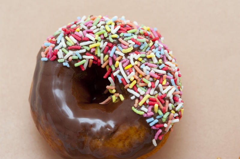 Delicious fresh chocolate ring donut with colorful sprinkles on a beige background with copyspace, overhead view