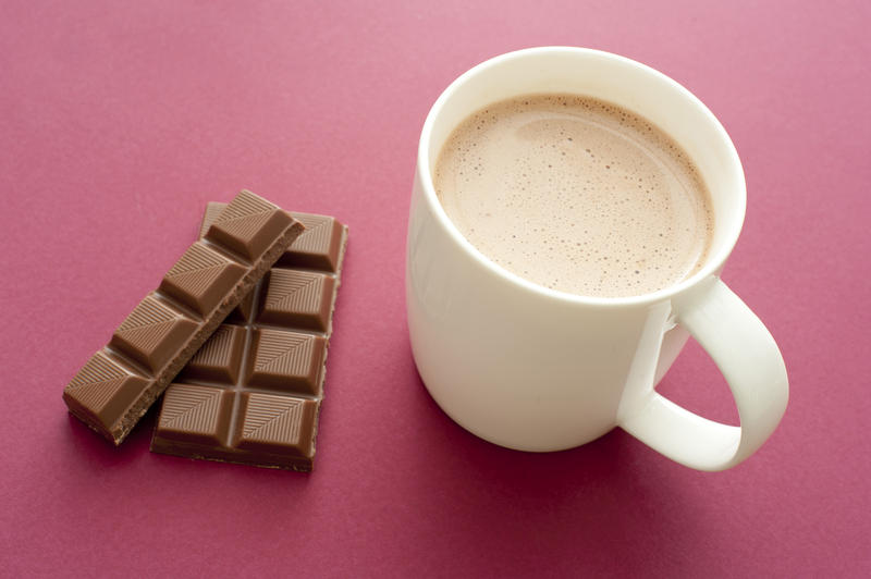 Delicious mug of hot chocolate drink with a partial bar of chocolate alongside used as an ingredient, high angle view over red