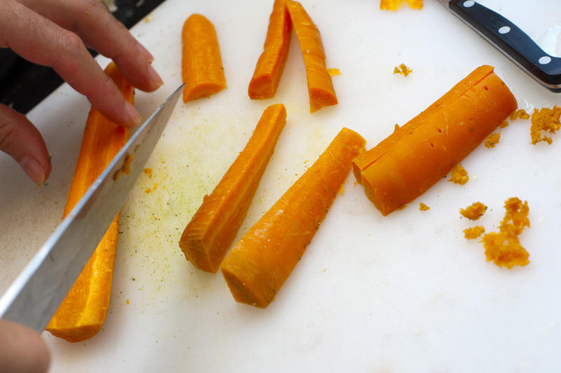 Hand of a man preparing fresh carrots scraping and cutting them into thin batons for use as a salad ingredient or as a cooked vegetable