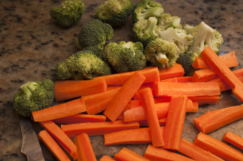 Chopped vegetables on a kitchen counter including carrot batons and broccoli pieces ready to be cooked as accompaniments to a meal