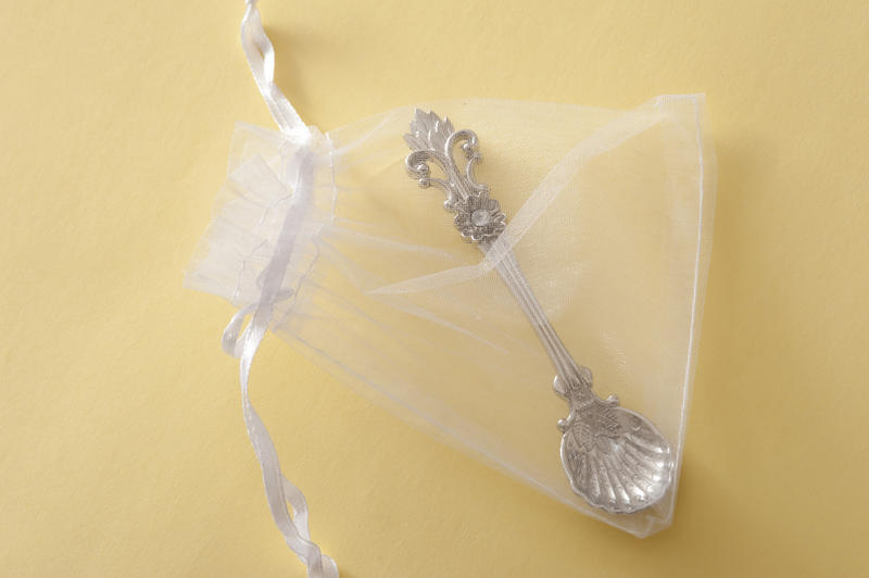 Ornate traditional silver christening spoon in a gift bag symbolic of luck and fortune for the baby over a neutral beige background