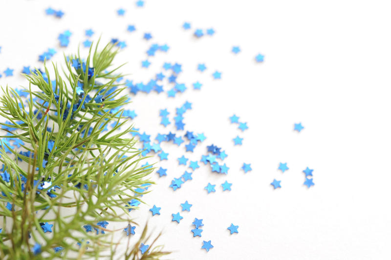 Christmas Backdrop Concept - Close up Fir Tree Branch on White Table with Small Blue Stars Particles.