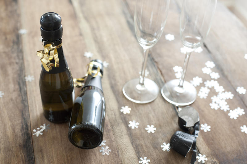 Two bottles of champagne decorated with Christmas ribbon with empty flutes alongside surrounded by scattered snowflake decorations conceptual of celebrating the festive season