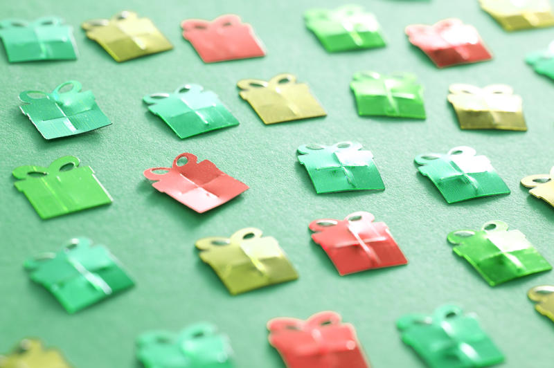 Christmas gift background with paper decorations in the shape of small gift-wrapped boxes scattered across a green surface viewed at an oblique angle