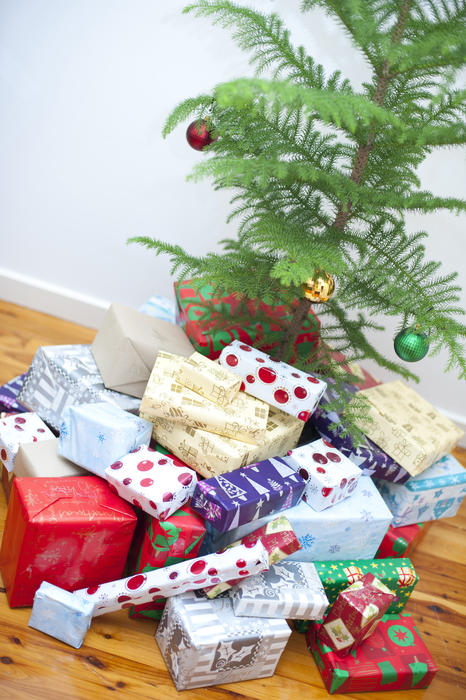 Large collection of colourful gift-wrapped Xmas presents gathered at the foot of the Christmas tree ready for a family celebration