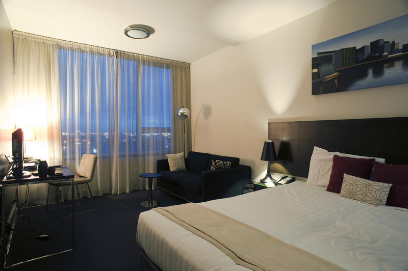 City bedroom with a large double bed , desk and a view through the curtained window of the city lights