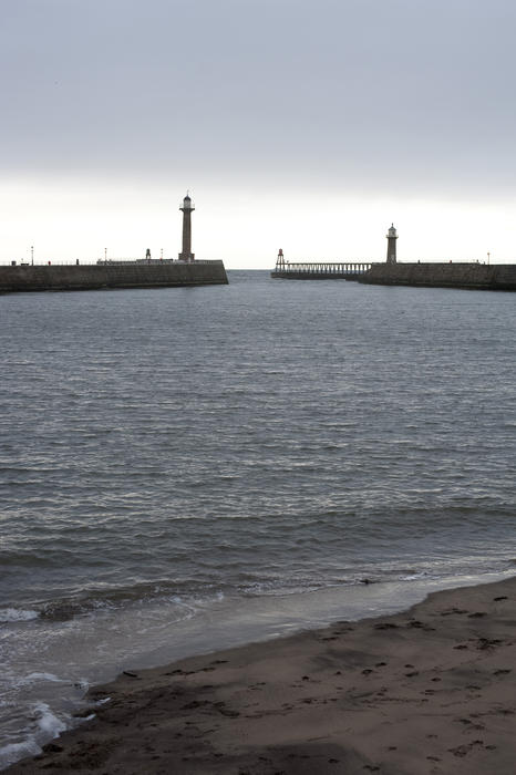 View across the calm water of Whitby harbour to the entrance with its navigation lights and stone piers