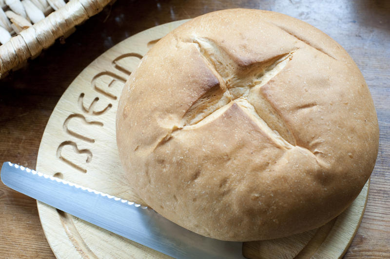 Traditional cob roll, a round crusty bread roll or loaf, standing ubcut on a wooden bread board