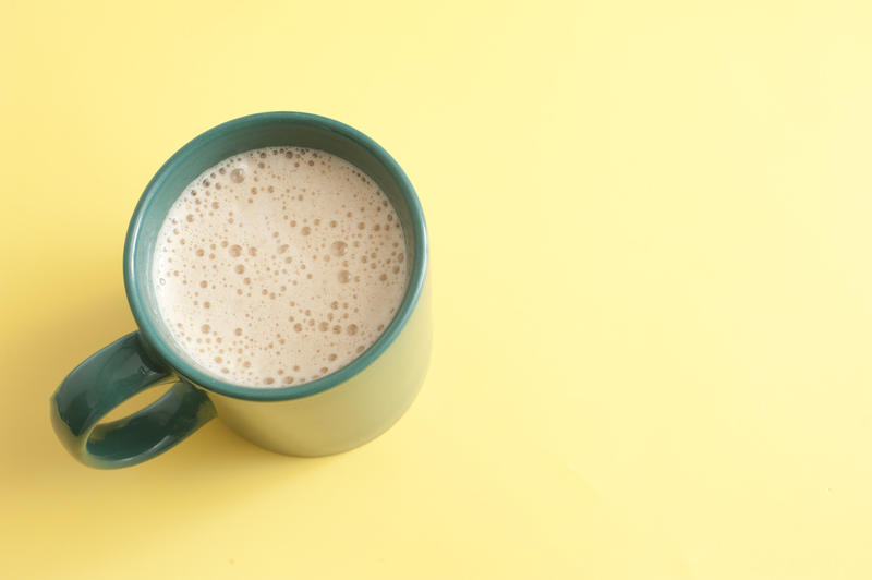 Mug of freshly poured frothy aromatic coffee or cappuccino for a refreshing coffee break viewed high angle on yellow with copyspace