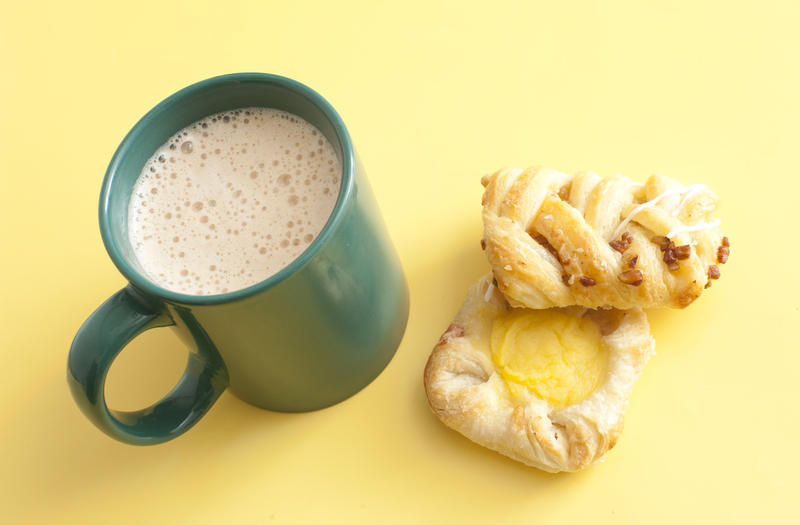 Coffee break with fresh biscuits or pastries and a freshly brewed frothy mug of hot refreshing coffee, high angle on yellow