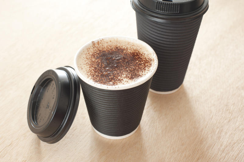 Hot frothy takeaway coffee in a disposable cup with the lid off to display the beverage, high angle view