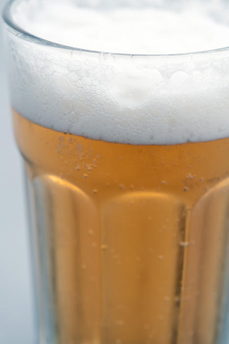 Glass of cold frothy beer with a close up partial view of the glass with condensation on the outside and effervescent bubbles in the lager, draft or beer