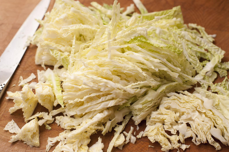 Preparing cabbage for a coleslaw salad with a heap of finely diced and sliced fresh cabbage on a wooden chopping board