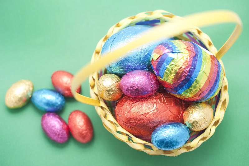 A display of coloured Easter Egg in their foil wrapping in and alongside a wicker basket