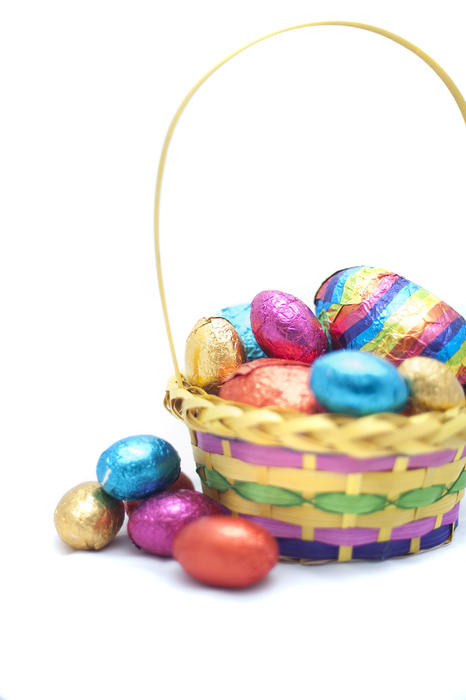 Colourful Easter Egg basket filled to overflowing with decorative shiny foil wrapped eggs on a white background