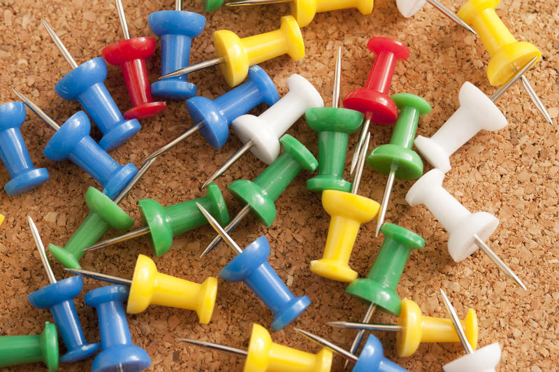 Close up Scattered Colorful Sharp Pins on Top of Brown Cork Board.