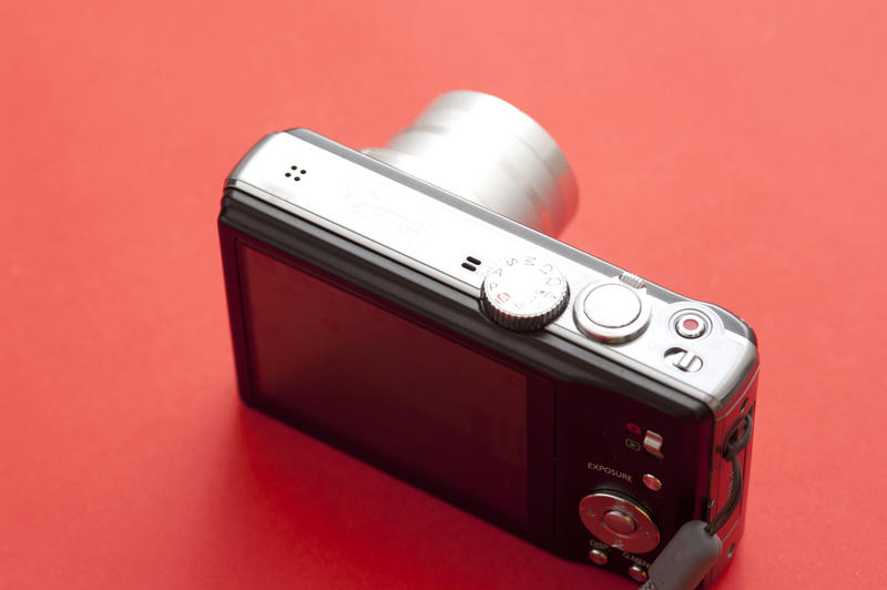 Overhead Rear View Still Life of Compact Digital Camera with Zoom Lens on Red Background