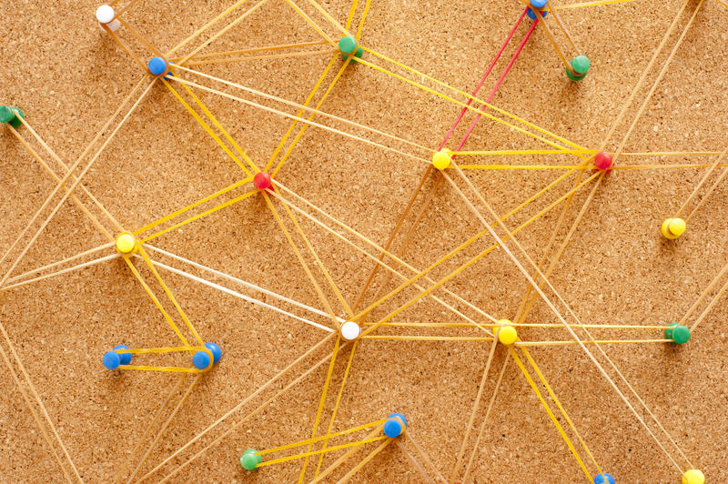 Networking Concept Using Colored Pins on Brown Cork Board Connected with Yellow Rubber Bands
