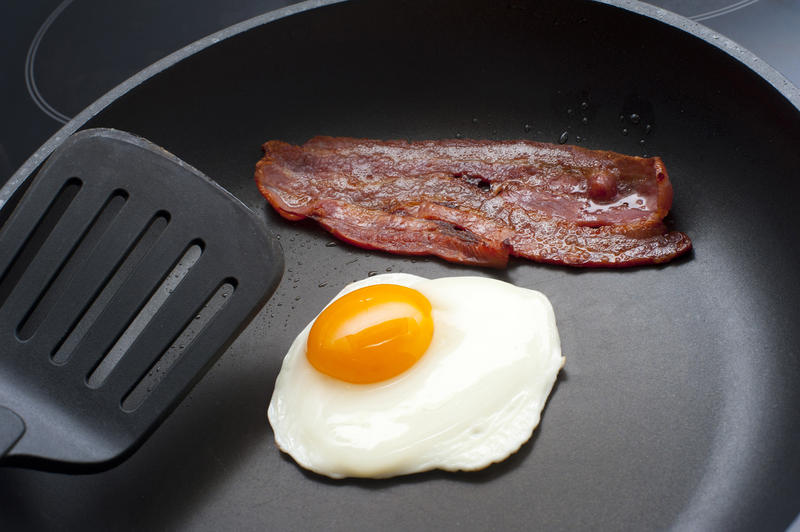 Frying an egg and crispy rasher of bacon for breakfast in a non-stick frying pan