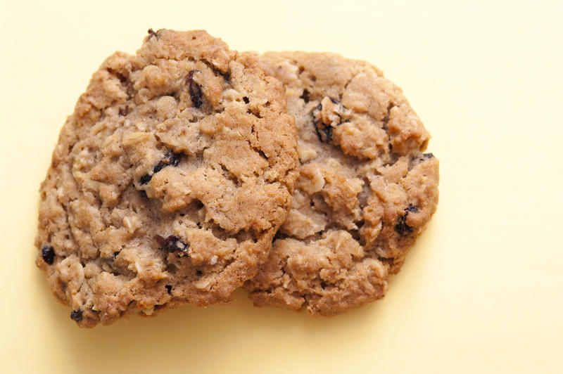Cookie treat with two delicious crunchy oat cookies or biscuits with raisins on a yellow background with copyspace