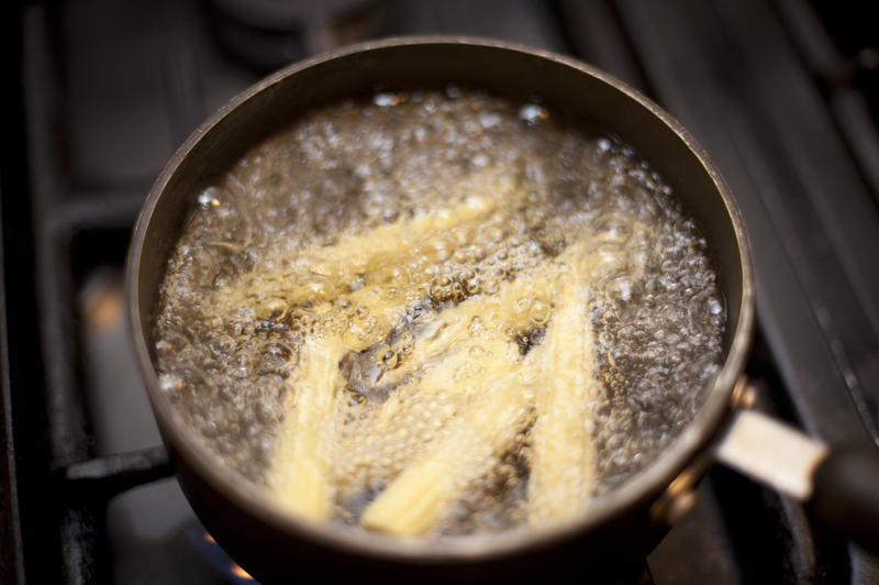 Cooking baby corn on the cob in a pot of boiling water with bubbles on a gas hob as a tasty vegetable accompaniment or salad ingredient