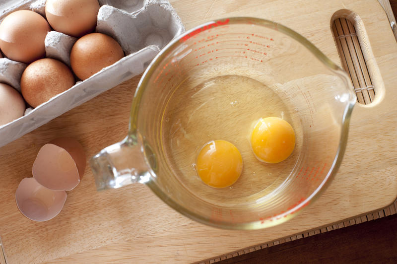 Overhead view of two cracked eggs with lovely yellow yolks in a glass measuring jug on a kitchen counter ready to be used as a baking ingredient