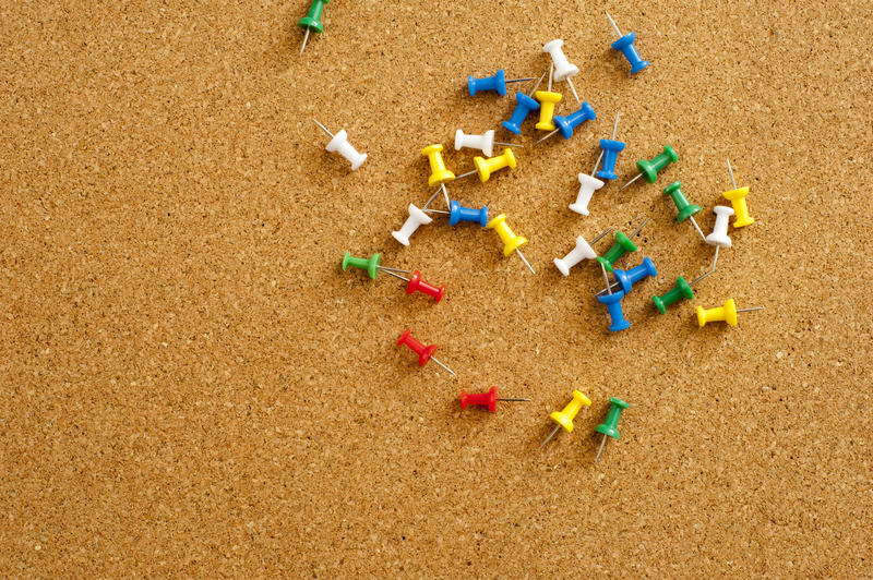 Plenty Colored Sharp Map Pins Scattered on Top of Brown Cork Board.