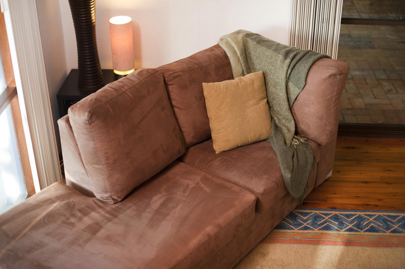 Comfortable day bed styled couch with a woollen throw and cushion in front of a window, high angle view